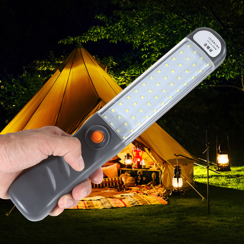 Hand met brandende LED-werklamp bij een tent op de camping in de avond
