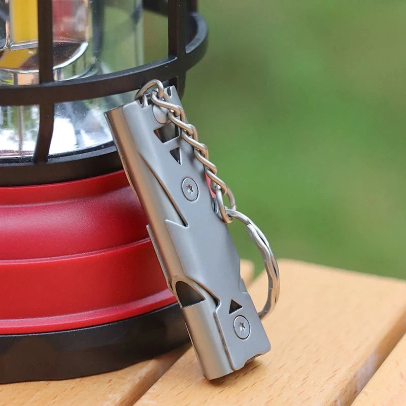Stainless steel emergency whistle on a key ring next to a lantern