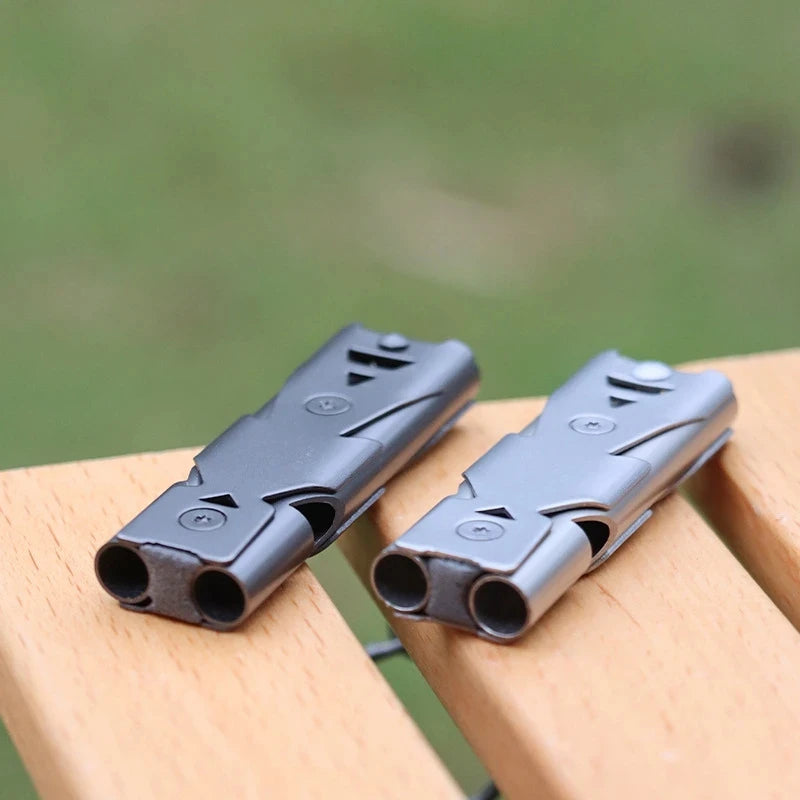 Two stainless steel emergency whistles on a wooden surface